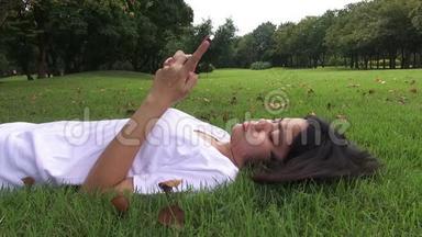 年轻女子躺在草地上发短信，在公园里发短信。